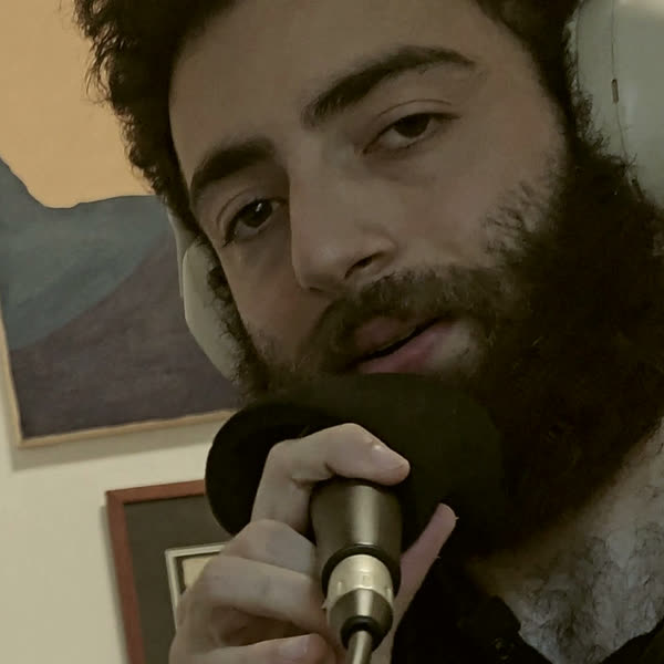 ori at the desk, headphones on, mic in hand, saying hello